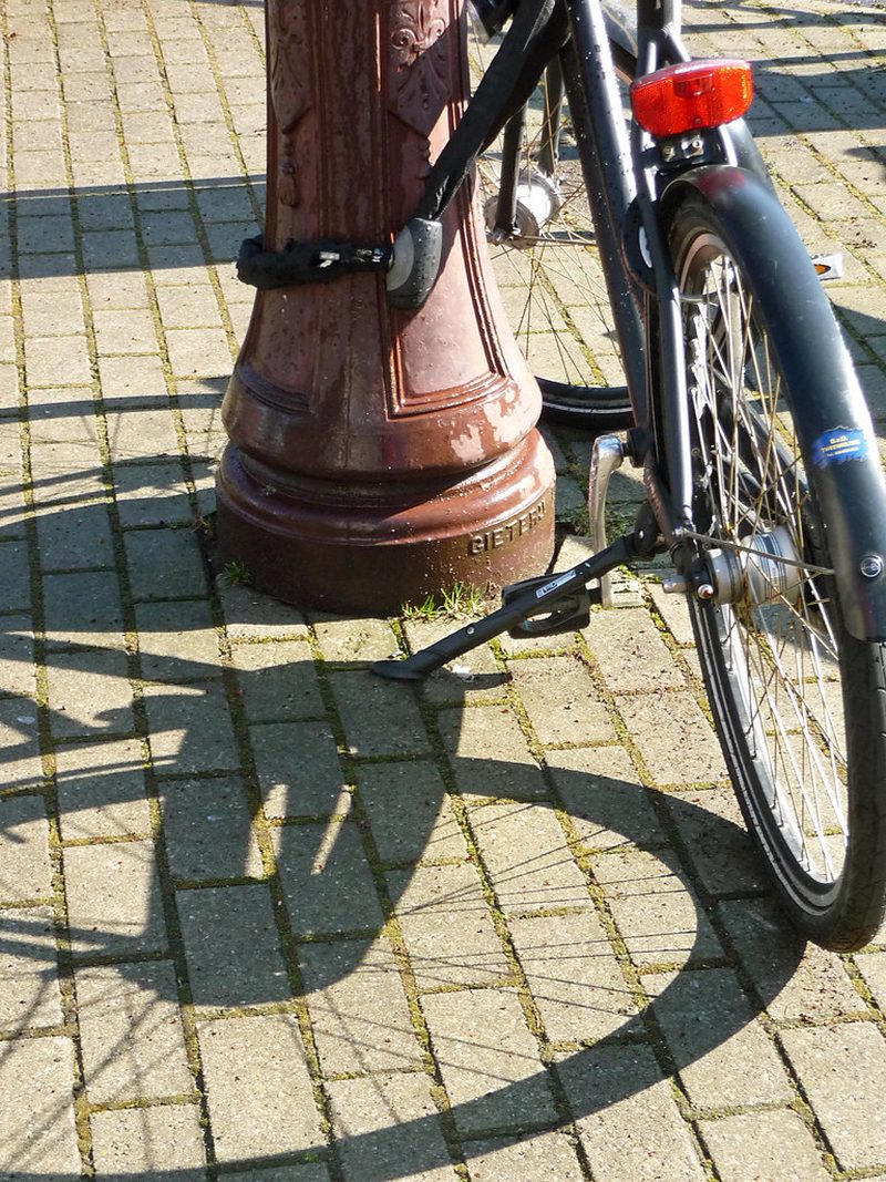 A bicycle locked to a bollard on a sunny brick pavement