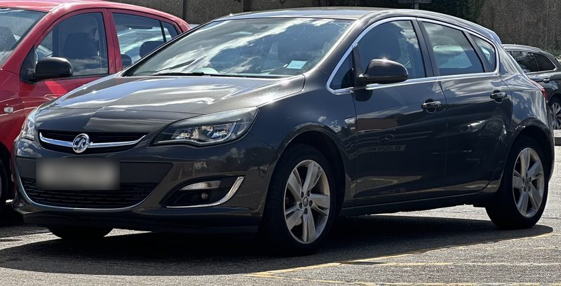 A dark grey hatchback parked in a car park, number plate blurred