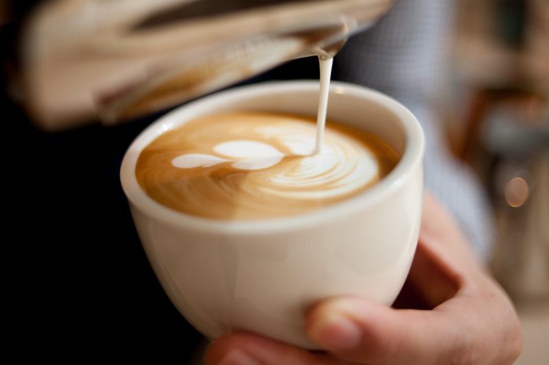 Milk being poured into a latte with a leaf pattern in the foam