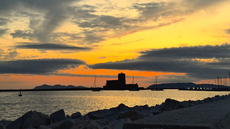 An orange sunset over a calm bay with a small stone fort on the shore